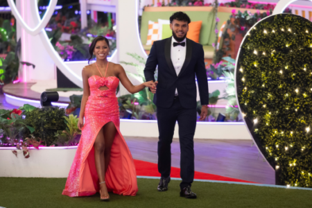 Amaya Bryan, a couple from Love Island USA, walk hand-in-hand on a red carpet, smiling.