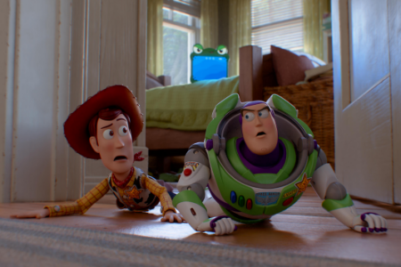 Woody and Buzz Lightyear from Toy Story crawl on a wooden floor with surprised expressions.