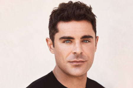 Headshot of actor Zac Efron with blue eyes, looking directly at the camera against a light background.