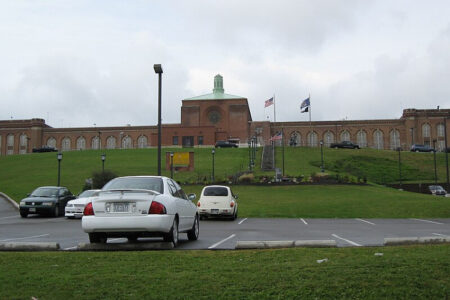Exterior view of Elmira Correctional Facility, a large brick building on a grassy hill with a parking lot in the foreground.