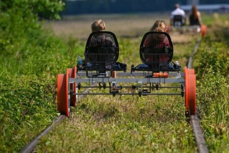 Two people ride a rail bike on overgrown tracks, with others in the distance, at the now-closed Penn Yan attraction.
