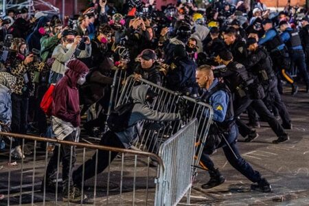 Police and protesters push against metal barriers during a violent demonstration at an immigration detention center.