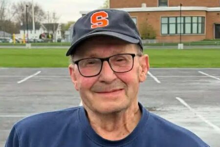 Smiling man Jim Patsos Jr. wearing glasses and a Syracuse University baseball cap.