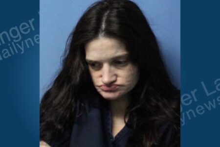 Mugshot of Jinny Easton, a woman with long dark hair, looking down with a slight frown against a blue background.