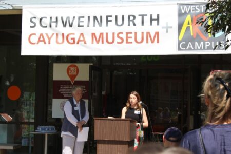 Woman speaks at podium outside Schweinfurth + Cayuga Museum, opening new exhibit on Cayuga Nation displacement.