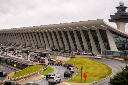 Exterior view of Washington Dulles International Airport terminal and control tower with cars on the arrival/departure ramps.
