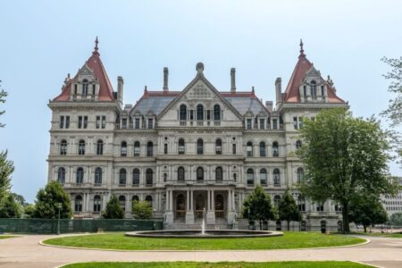 The New York State Capitol building in Albany, a grand stone structure with red roofs and a fountain in front.