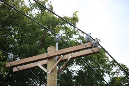 RG&E utility pole with power lines and a wooden crossarm against green trees, related to power restoration.