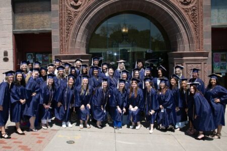 Group of 39 Finger Lakes Health nursing graduates in caps and gowns smiling outside a building.