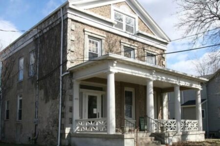 A two-story building with a stone facade and a white columned porch, identified as the Ontario County Homeless Shelter.