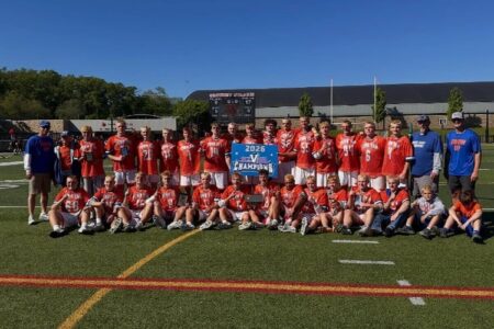 Penn Yan Lacrosse team celebrates their 29th sectional title on a sunny field, holding a '2026 V CHAMPIONS' banner.