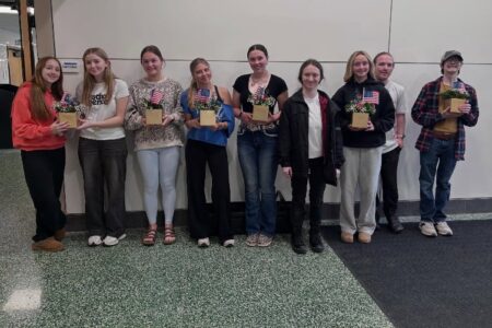 Pal-Mac students holding Memorial Day centerpieces with flowers and American flags in a school hallway.
