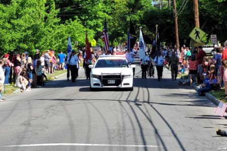 A police car leads a Memorial Day parade with flag bearers and spectators lining the street in Penn Yan.