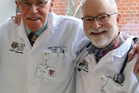 Doctors Roger Platzer and Mark Equinozzi, wearing lab coats, smile with arms around each other.