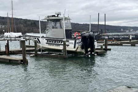 Schuyler County Sheriff boat docked on a lift at a marina on Seneca Lake under an overcast sky.