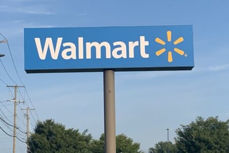 A blue Walmart sign with white text and a yellow starburst logo against a clear blue sky.