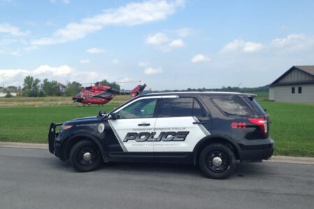 A Seneca Falls Police SUV is parked on a street with a red medical helicopter visible in the grassy background.