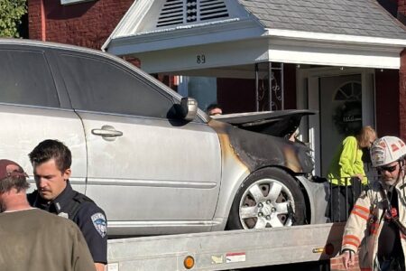 A fire-damaged silver car is loaded onto a tow truck, with a police officer and firefighter nearby at a Seneca Falls scene.
