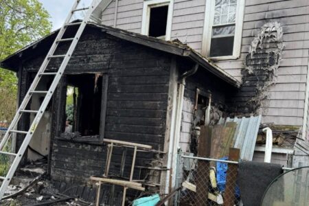 A house in Sodus Point heavily damaged by fire, with a charred exterior and a ladder leaning against it.