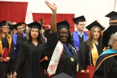 Smiling graduate TQueria Bowman waves during Cayuga Community College's commencement ceremony.