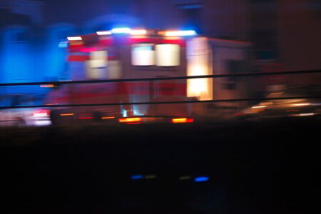 An ambulance with flashing lights speeds through the night, blurred by motion.