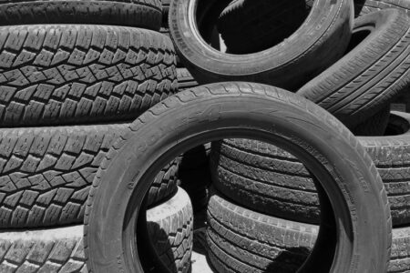 Black and white photo showing multiple stacks of used car tires, ready for recycling.