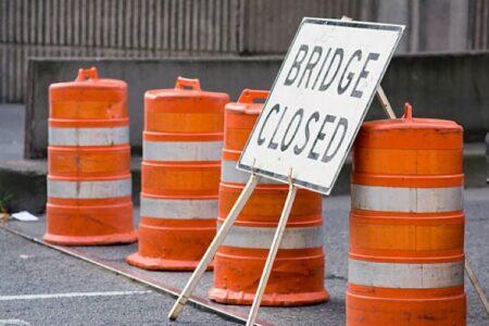 A 'BRIDGE CLOSED' sign stands among orange traffic barrels on a road, indicating a closure.