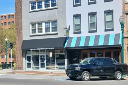 Exterior of Cellar + Folly Whiskey Company storefront in downtown Auburn, NY, with a black truck parked outside.