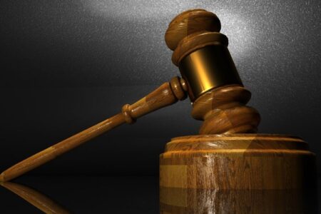 A wooden court gavel rests on its sound block, symbolizing law and justice against a dark background.