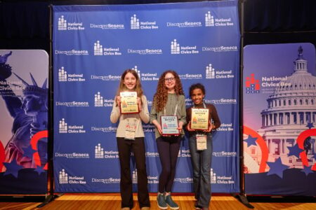 Three students proudly hold awards at the National Civics Bee, standing in front of a blue backdrop with event logos.