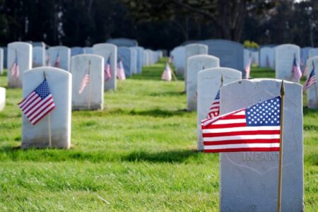 Rows of white gravestones with American flags in a military cemetery.
