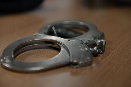 A pair of metal handcuffs rests on a wooden table, symbolizing arrest and law enforcement.