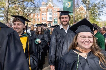 Smiling Keuka College graduates in caps and gowns walk during their commencement ceremony on campus.