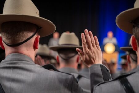 New York State Police recruits raise hands during a graduation ceremony, taking an oath.