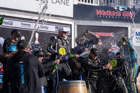 SVG and team celebrate victory in Watkins Glen's Victory Lane, spraying champagne.