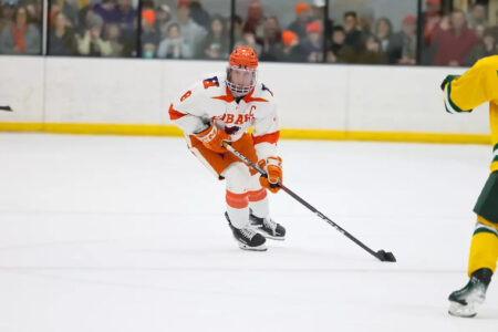 Hobart Hockey Captain Daniels in white and orange skates with the puck during a game.