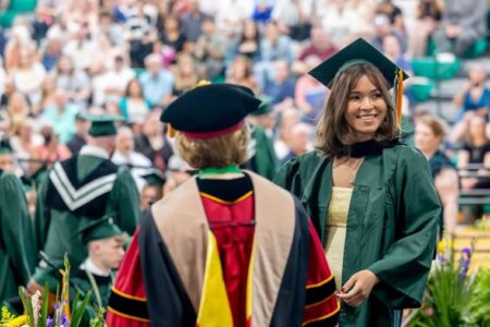 Smiling graduate in green cap and gown receives diploma from academic official at TC3 ceremony.