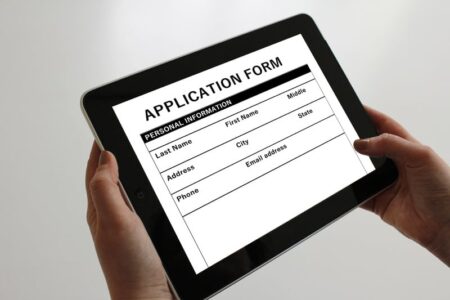 Hands hold a tablet displaying an online application form, representing financial aid applications like FAFSA or TAP.