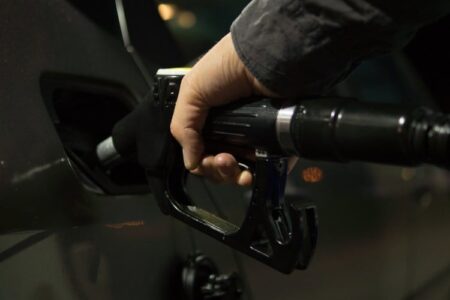A person's hand holds a gas pump nozzle, filling a car's fuel tank at night.
