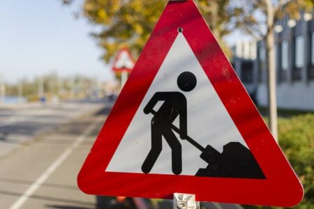 A red triangular road sign with a black silhouette of a person digging, indicating road work ahead.