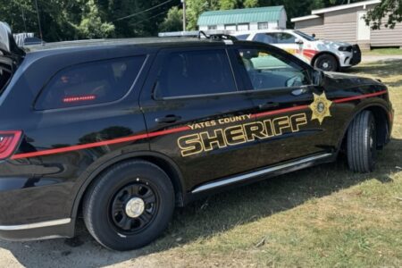 A black Yates County Sheriff SUV with gold lettering and a red stripe parked on grass.