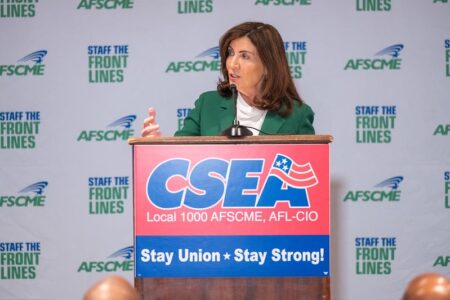 New York Governor Kathy Hochul speaks at a podium with CSEA and AFSCME logos, announcing a contract agreement.