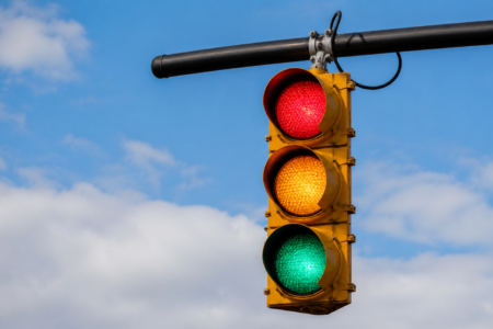 A traffic light with all three lights (red, yellow, green) illuminated against a blue sky with clouds.