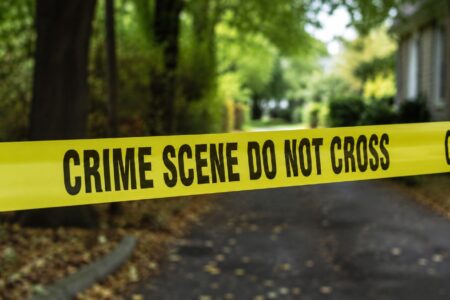 Yellow crime scene tape with 'CRIME SCENE DO NOT CROSS' stretched across a blurred outdoor background.
