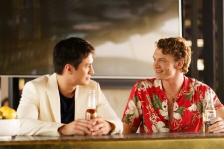 Two men, one in a blazer and one in a Hawaiian shirt, smile and talk at a bar.