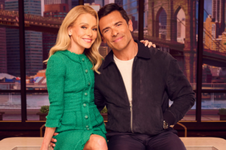 Kelly Ripa in a green dress and Mark Consuelos in a dark jacket pose smiling with a city skyline background.