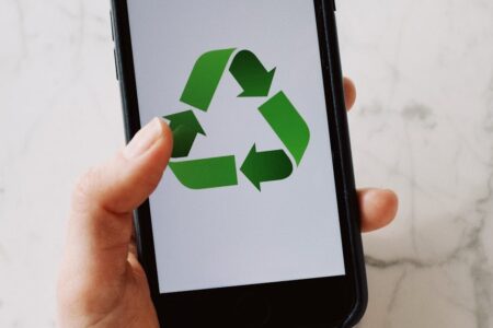 A hand holds a smartphone displaying a green recycling symbol on its screen.