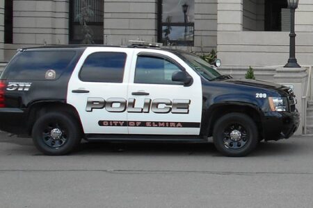 An Elmira Police Department cruiser, black and white, parked in front of a stone building.