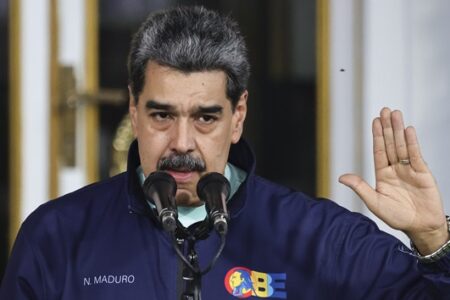 Venezuelan President Nicolas Maduro speaks at a podium, raising his right hand.