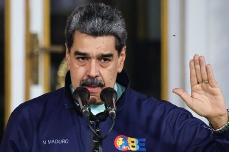 Venezuelan President Nicolas Maduro speaks at a podium, raising his right hand.